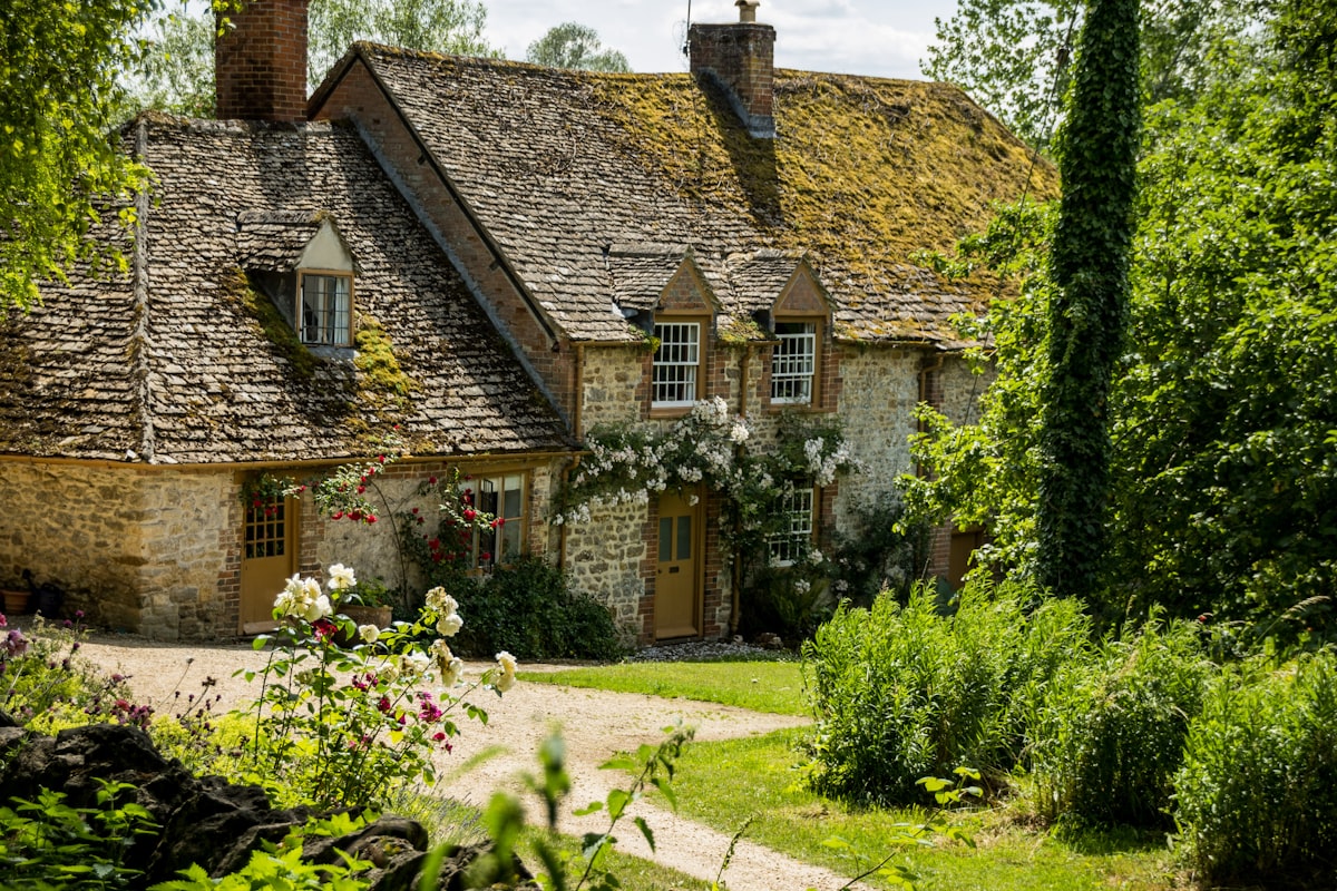 Stone cottage in Devon with moss-covered tile roof, red roses on the walls